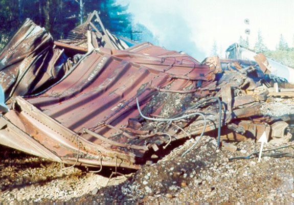 Figure 10 - Impact damage to box car CN 413849 as viewed looking west from crater in right-of-way. Arrow points to centre sill which was bent 90 degrees to the north