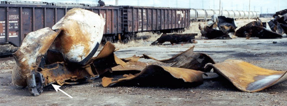 Figure 11 - Main part of the B end of the car, including the head and approximately 16.5 feet of the flattened sections of the tank shell recovered after the derailment. (The coupler and stub sill are in the foreground at the lower left). The remaining pieces of the tank car and jacket can be seen in the right background.